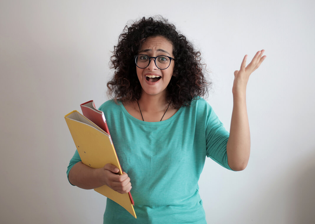woman in green shirt wearing glasses and holding files, looking confused - photo by Andrea Piacquadio on Pexels