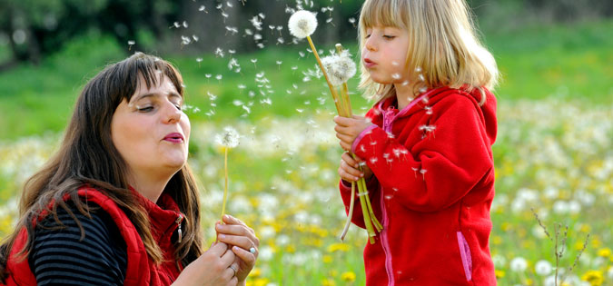woman and young girl blowing dandelion seeds 