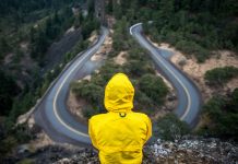 person in yellow jacket sitting at winding road overlook - photo by Justin Luebke on Unsplash