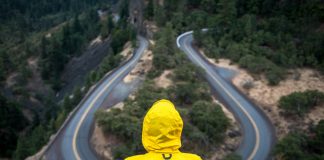 person in yellow jacket sitting at winding road overlook - photo by Justin Luebke on Unsplash