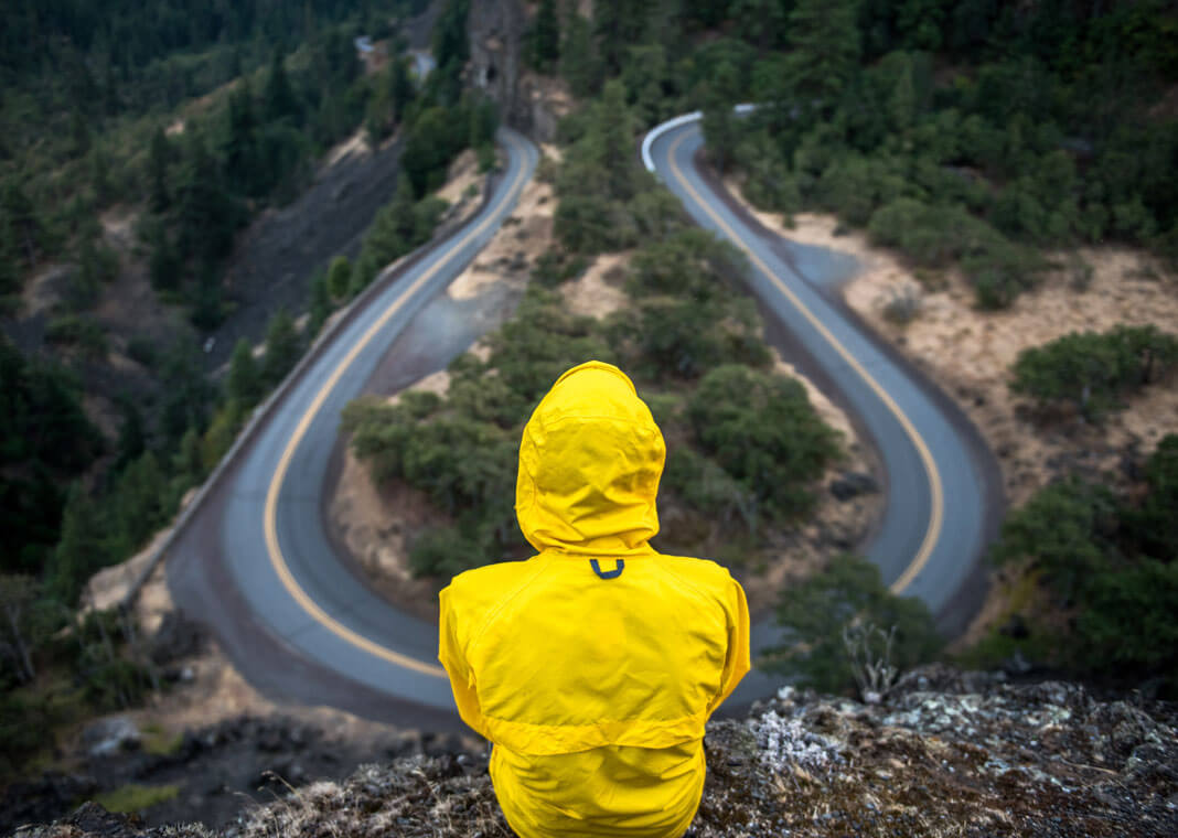person in yellow jacket sitting at winding road overlook - photo by Justin Luebke on Unsplash