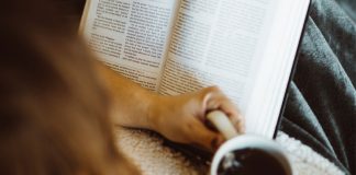 woman praying with Bible while drinking coffee