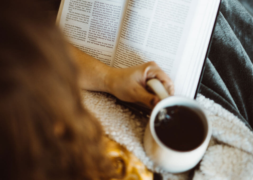 woman praying with Bible while drinking coffee