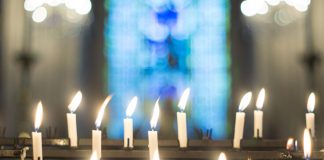 candles in front of blurry stained glass window - ImageJournal-Photography/Moment/Getty Images