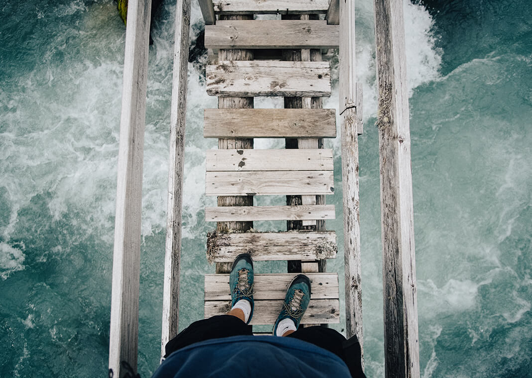 fearless person standing on wooden bridge over raging waters - photo by Benjamin Davies on Unsplash