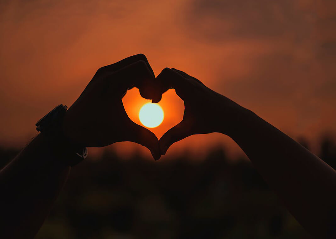 hands held in heart shape around sun in distance - photo by Shera Banerjee on Pexels