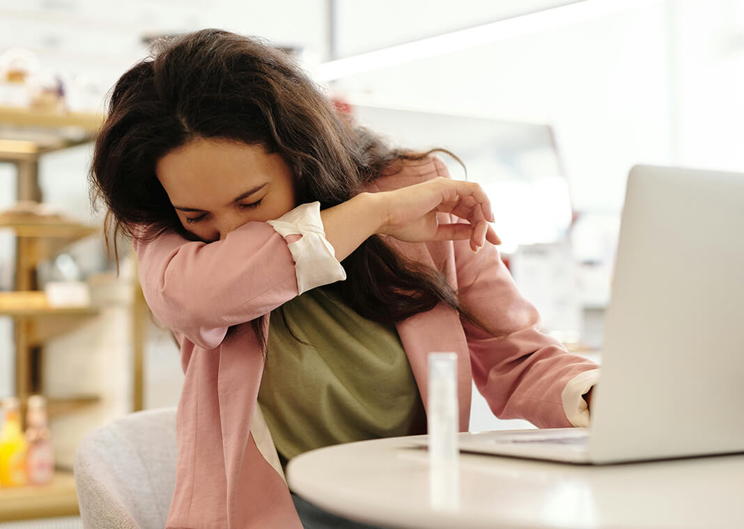 woman at laptop covering her sneeze with her arm - photo by Edward Jenner on Pexels.com