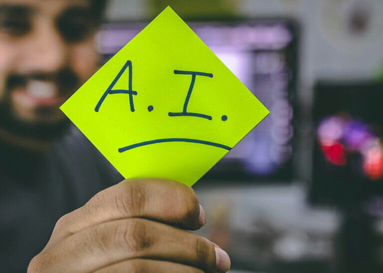 man in front of computers holding sticky note that says, "AI" - photo by Hitesh Choudhary on Unsplash