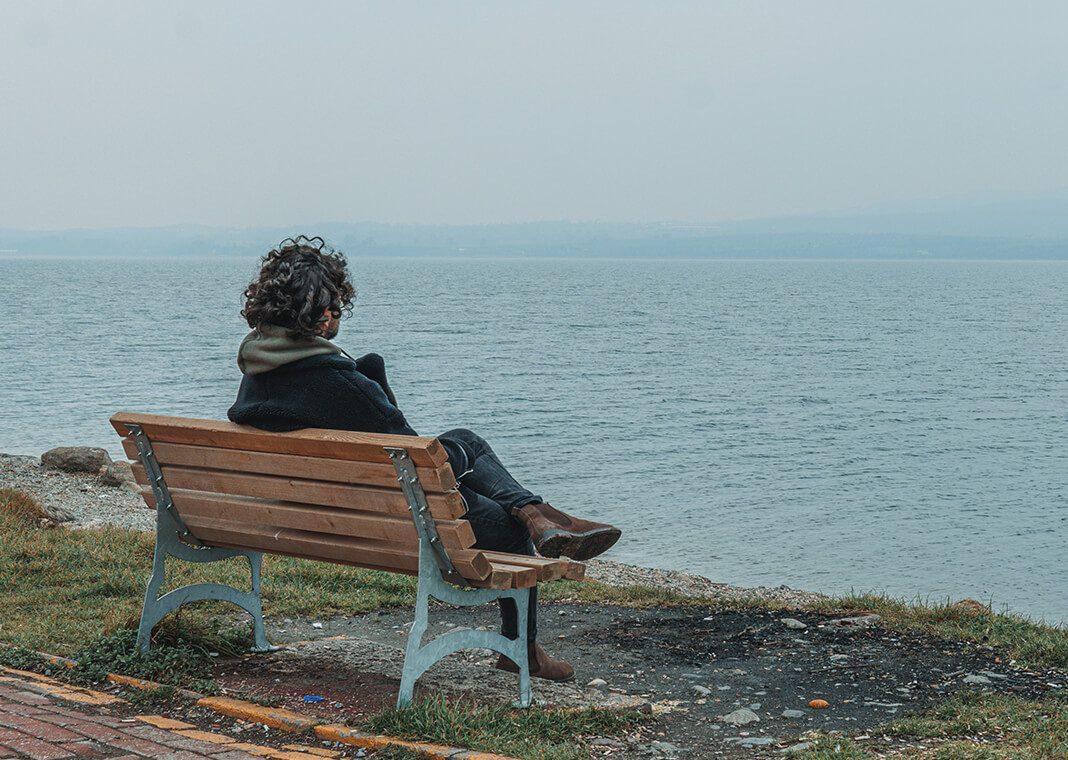 person sitting on a bench by water, daydreaming - photo by Mert Kahveci on Unsplash